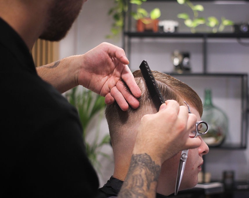 Barber shaping a fade with scissors and comb